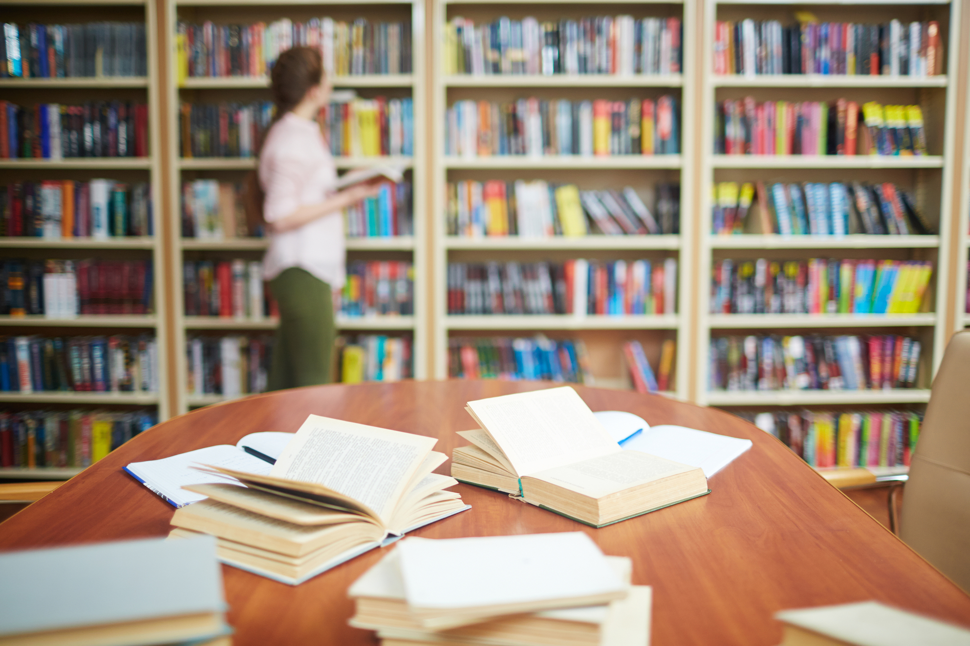 Open books on desk and human by bookshelf on background