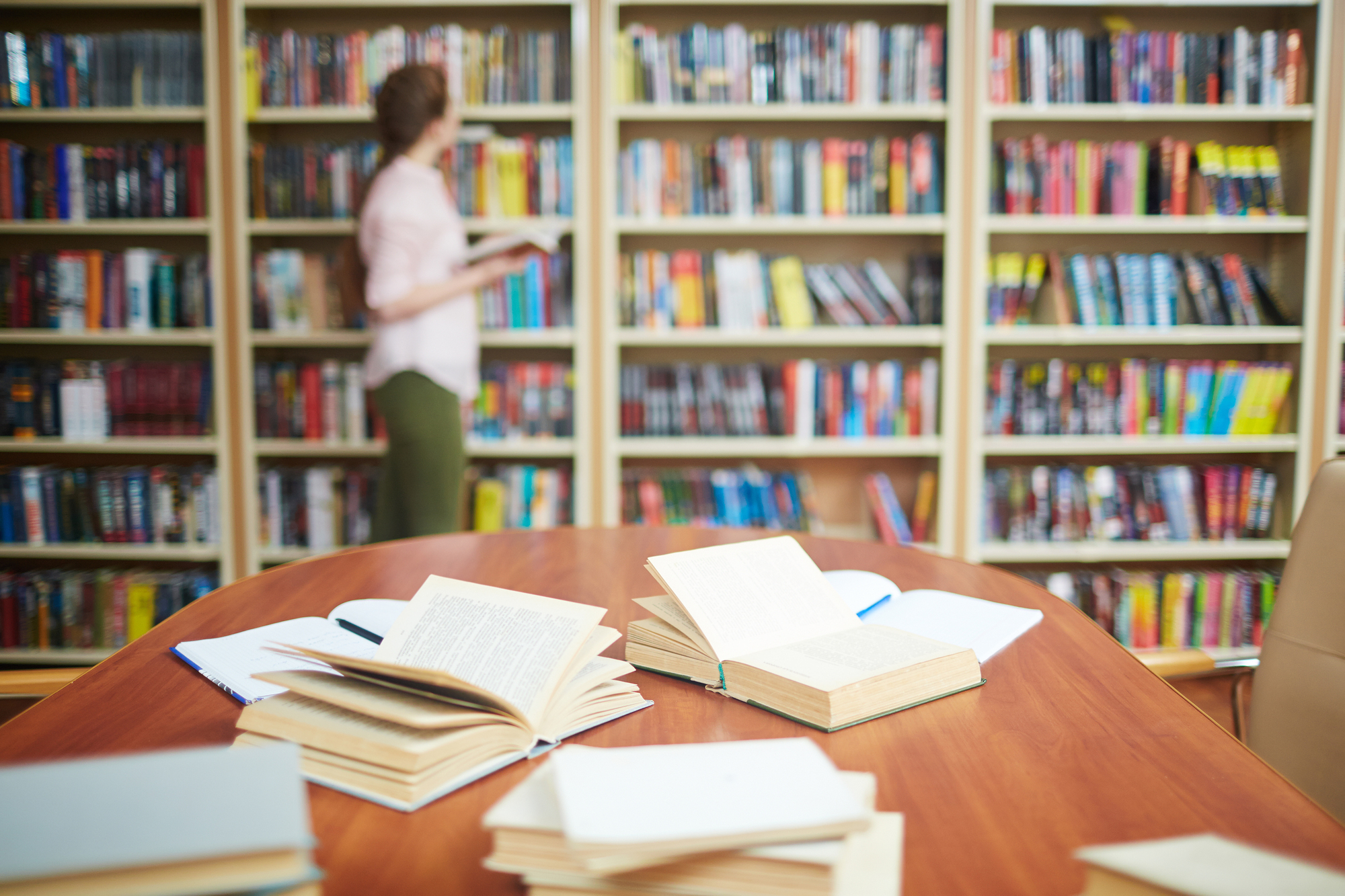 Open books on desk and human by bookshelf on background