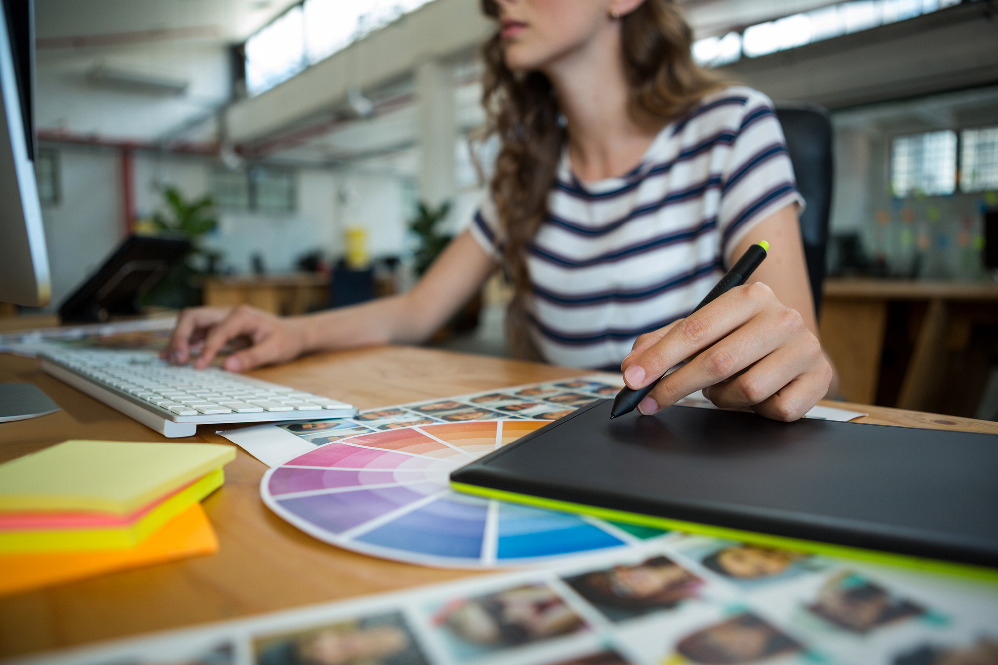 Mid section of female graphic designer using graphics tablet at desk in office