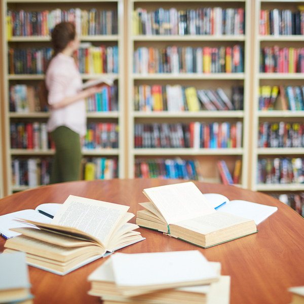Open books on desk and human by bookshelf on background